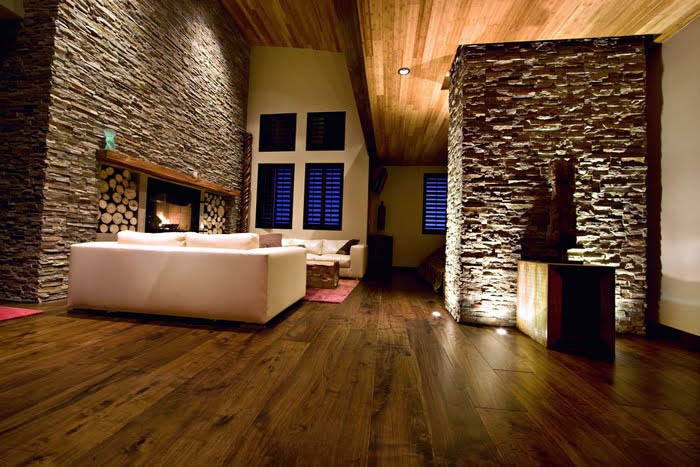 warn and dark-lit living room space with stone and brick features on wall and fireplace. White sofa in the room with lighting features highlighting art and space.