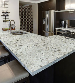Granite slab kitchen countertops with gray, white, and black specs. Stainless steel appliances in back.