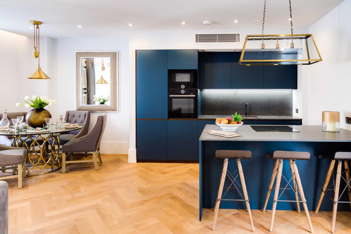jewel-tones, blue kitchen cabinets with chevron wood flooring and white walls, breakfast table in corner